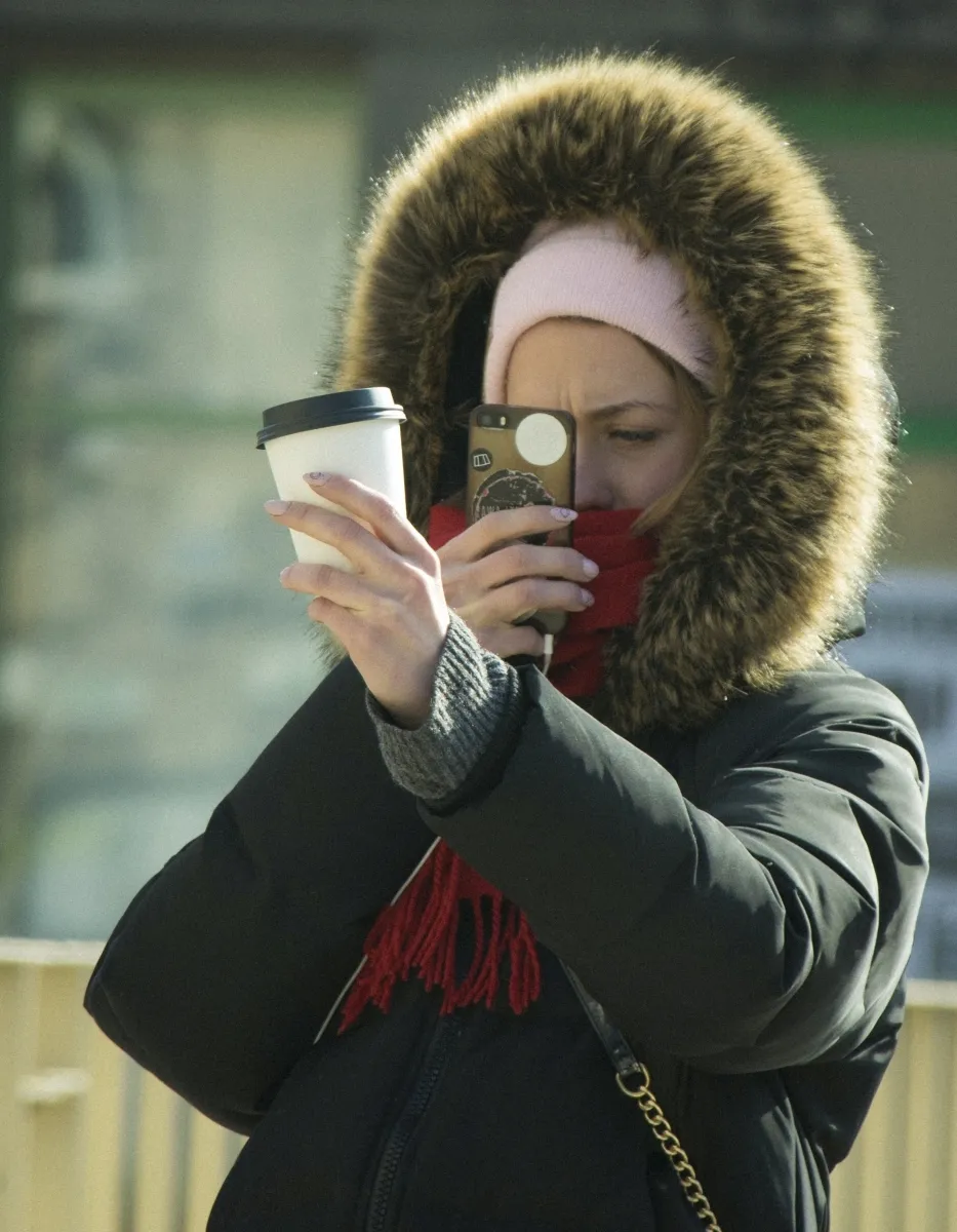 Woman in a fur hood taking a selfie while holding a takeaway cup
